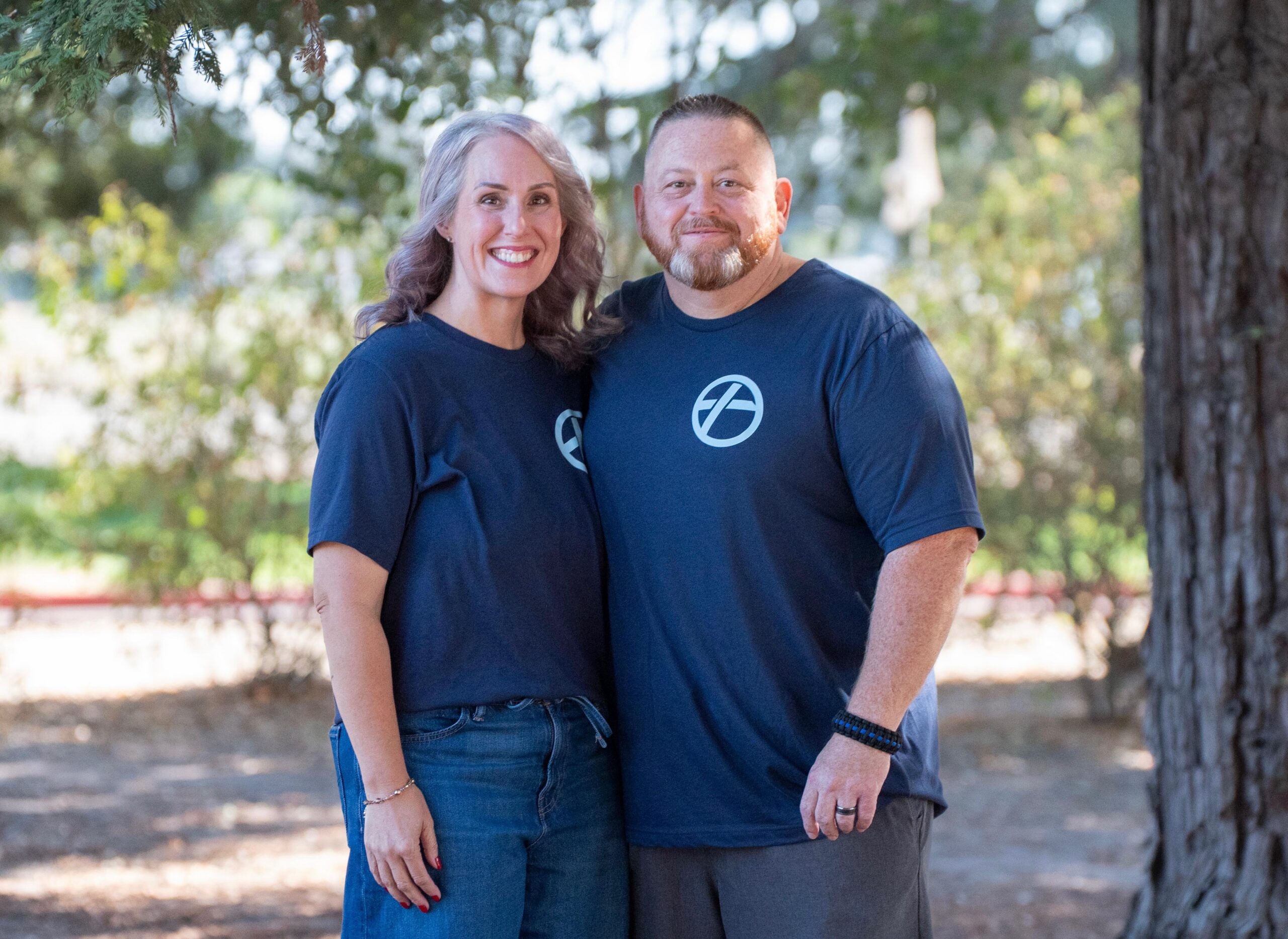 A married couple smiling together outdoors, both wearing Shelter Cove t-shirts