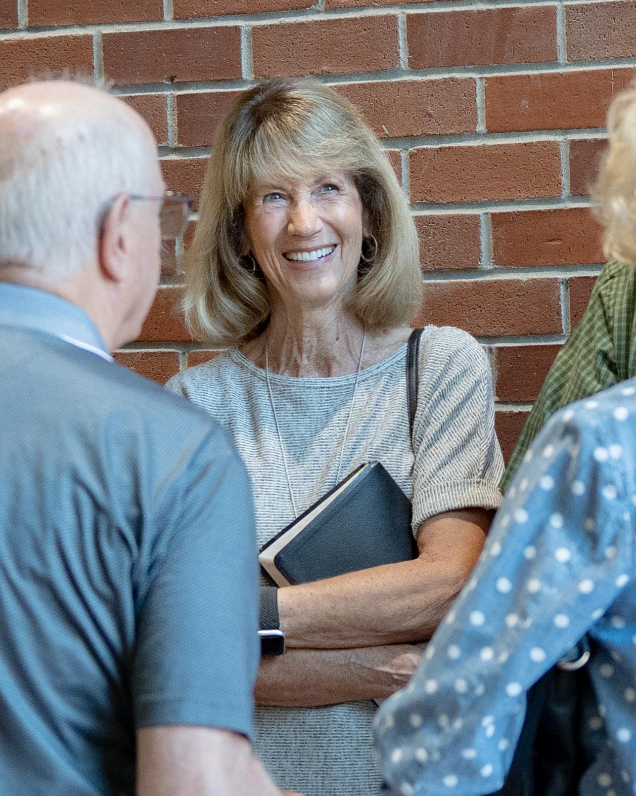 A woman smiling while talking with others and holding a Bible