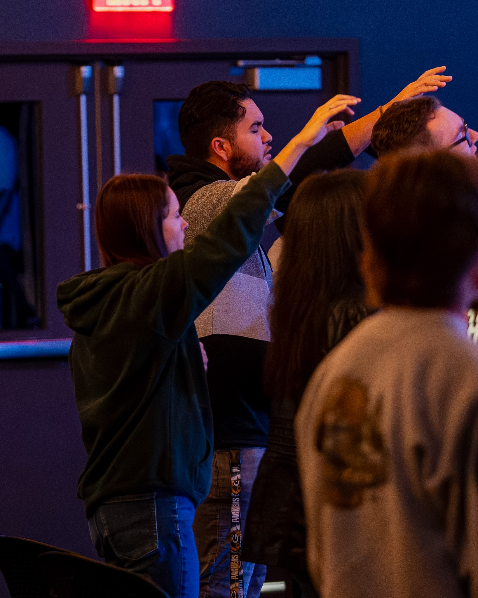 Young adults raising their hands in worship during a Young Adults gathering