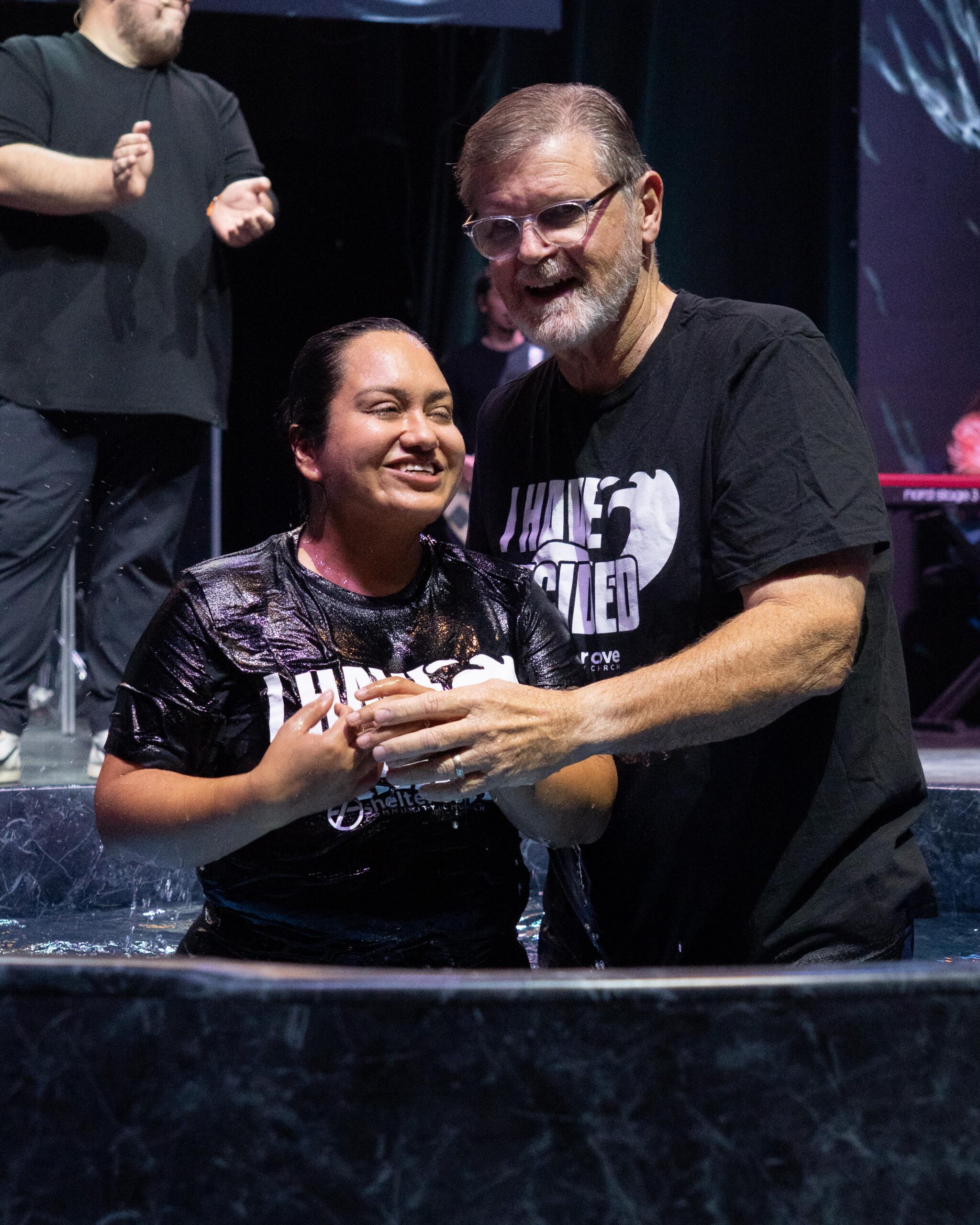 Two people standing together in the baptism tub, smiling after a baptism at Shelter Cove