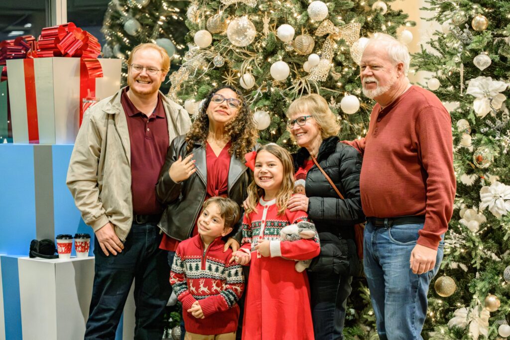 A family with kids in Christmas sweaters in front of the Christmas tree